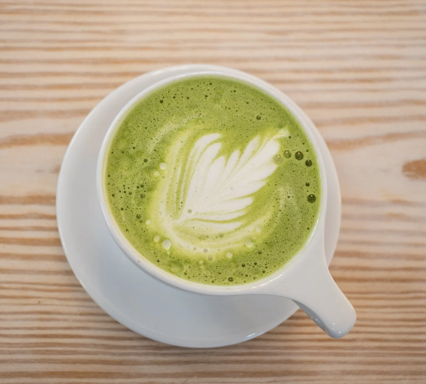 A matcha latte in a white porcelain cup on a wooden table at Café Meria