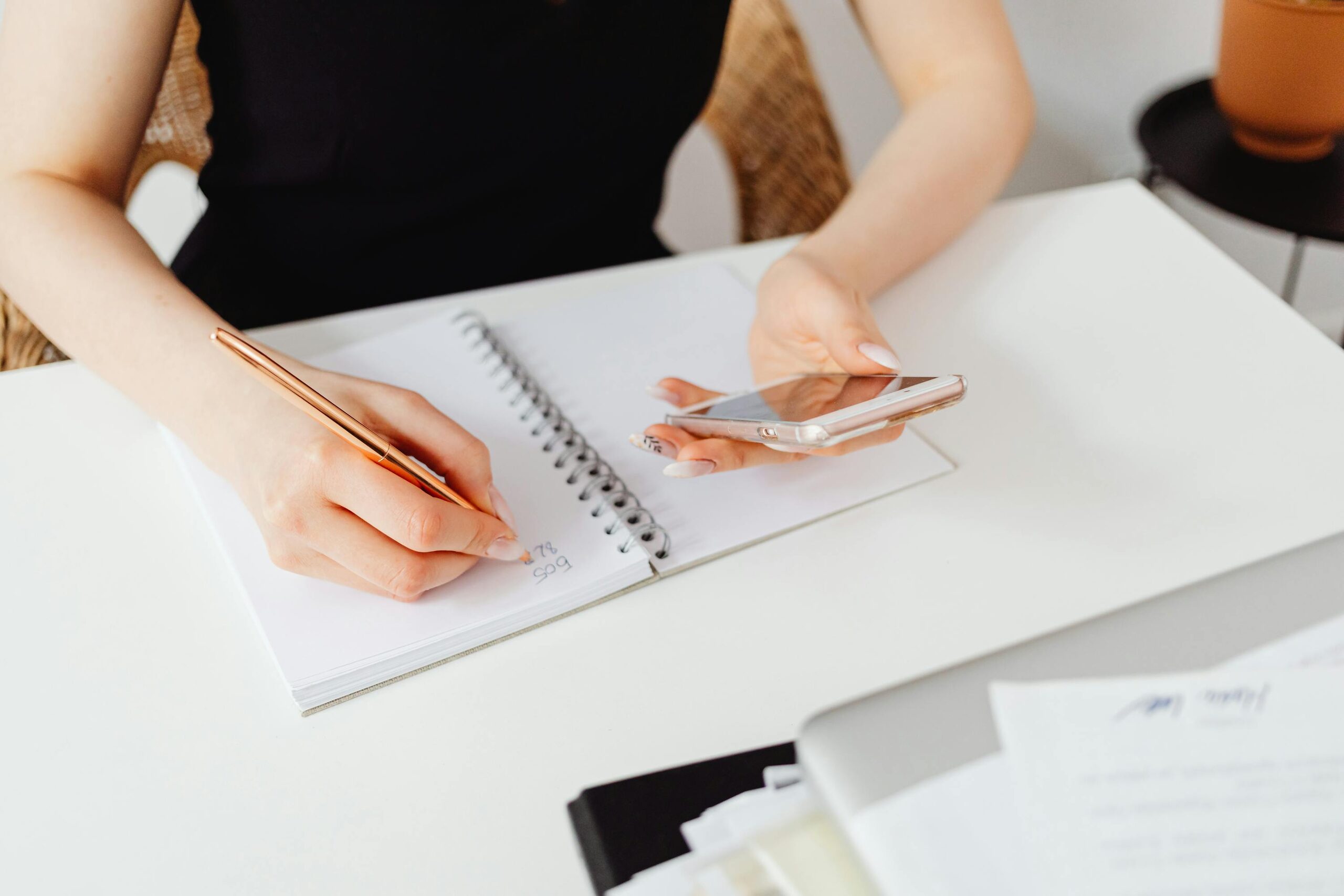 Hands holding a smartphone over an open spiral notebook in soft natural light — the calm planning posture Composed is built for