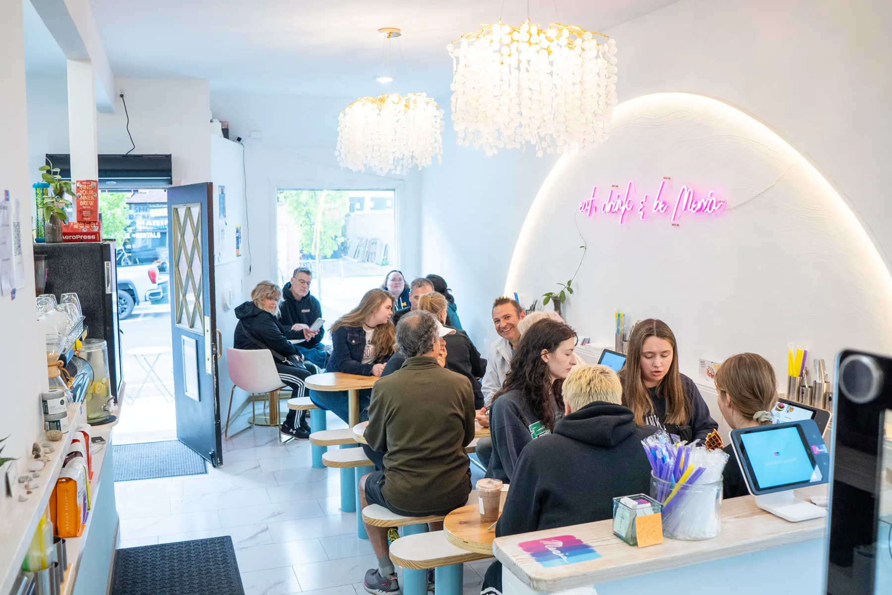 Café Meria on a full morning: friends at every table under the pink neon arc